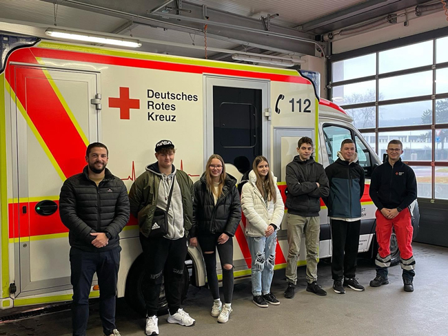 Schüler des Wahlpflichtkurses Feuerwehr mit Lehrer Jonas Seitz und Dennis Gleim vom Rettungsdienst des DRK vor einem Rettungswagen