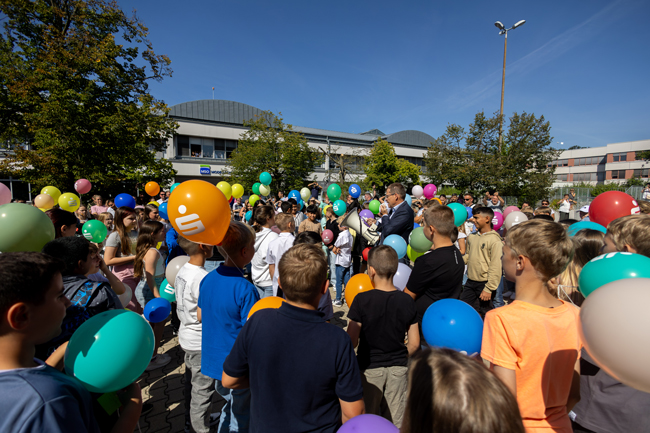 Herr Stückradt, inmitten von Schülern mit Luftballons auf dem Schulhof, hat ein Megafon in der Hand