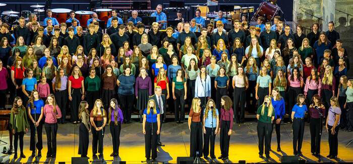 Chorschüler in bunten T-Shirts singen auf großer Bühne