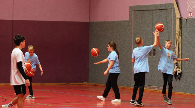 Schüler, die in einer Halle mit vielen Bällen Basketball spielen