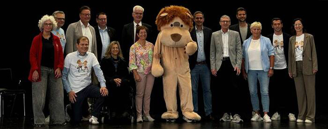 Gruppenbild von erwachsenen Personen und einer Person in großem Plüschlöwen-kostüm