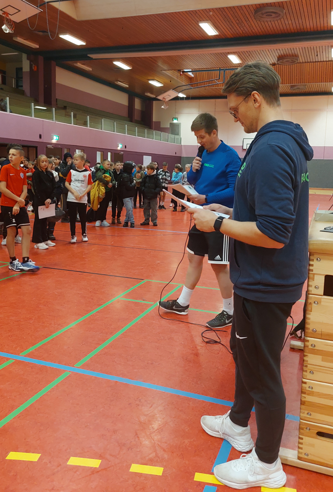 Sportlehrer bei Urkundenübergabe mit Mikro in der Hand