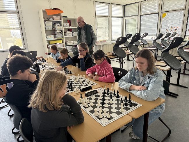 Schüler sitzen sich gegenüber an Tischen auf denen Schachbretter stehen und schauen konzentriert auf die Schachfiguren