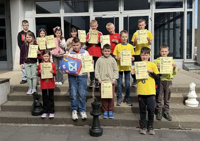 Gruppenbild der Sieger des Schulschachwettbewerbs auf Treppenstufen vor der Schule mit Urkunden in den Händen