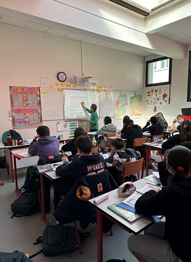 Blick in einen Klassenraum, Lehrerin schreibt etwas an Tafel