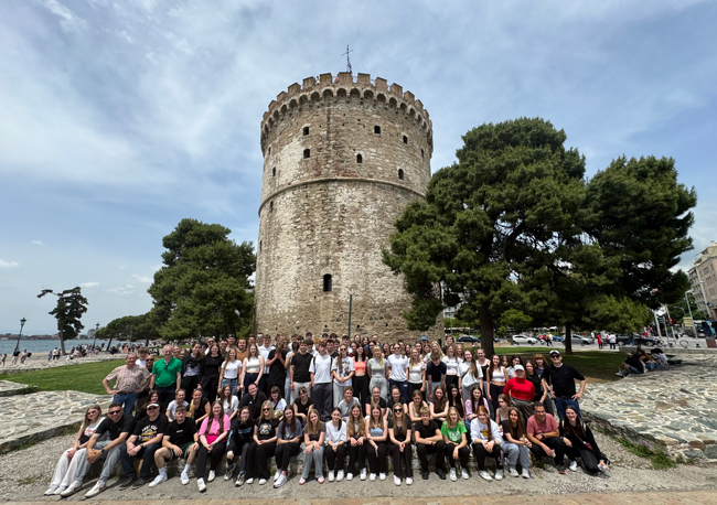 Gruppenbild Chorschüler vor einem großen Turm aus Stein, rundherum Bäume, im Hintergrund Meer