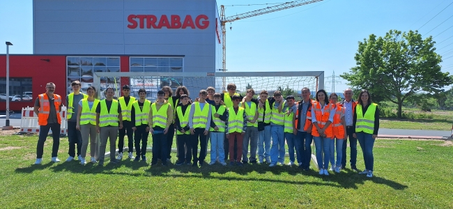 Schülergruppe mit Lehrern vor einer großen Produktionshalle mit Aufschrift STRABAG