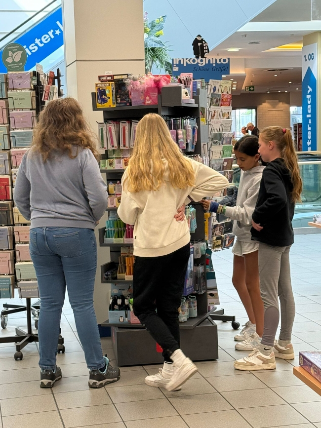 Schüler von hinten stehen vor einem Regal in der Buchhandlung