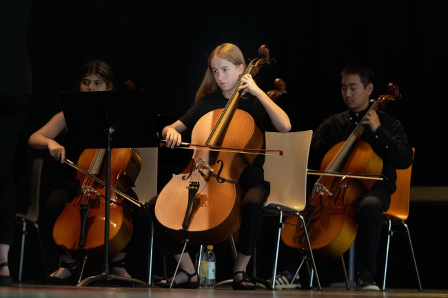 Schüler an großen Streichinstrumenten auf der Bühne spielend
