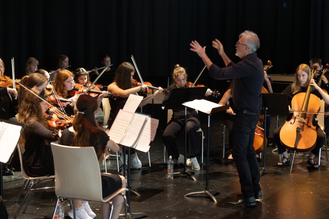Dirigent vor sitzenden Schülern, die auf Streichinstrumenten spielen