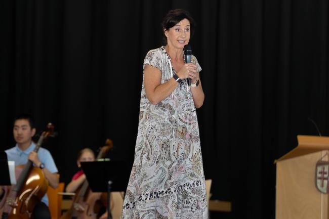 Schulleiterin in langem Blumenkleid spricht zum Publikum