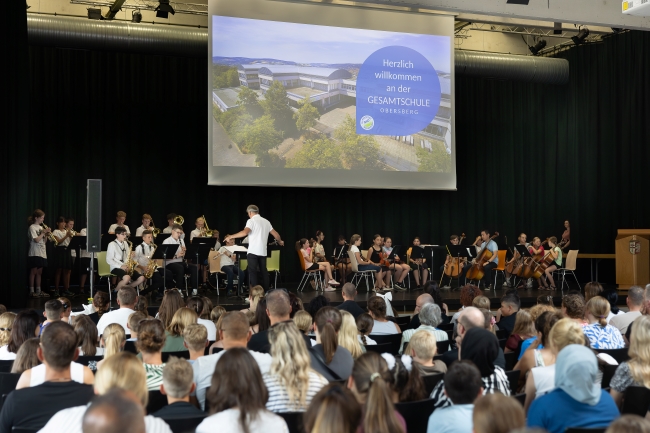 Publikum von hinten mit Blick auf Bühne, wo Musiker dirigiert werden