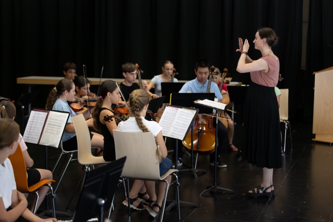 Lehrerin dirigiert musizierende Streicher auf der Bühne