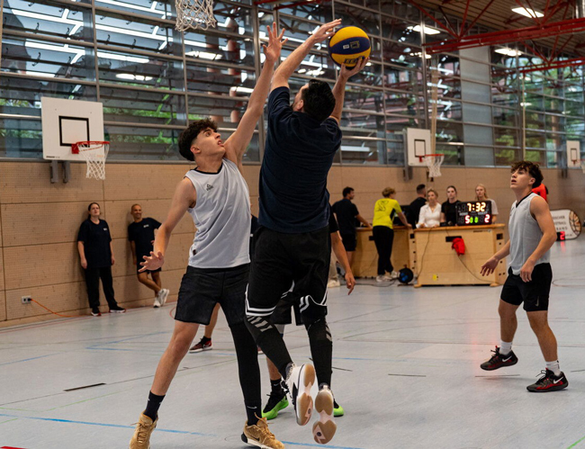 Basketballspieler einer gegenerischen Mannschaft von hinten, GSO-Schüler versucht Wurf zu blocken