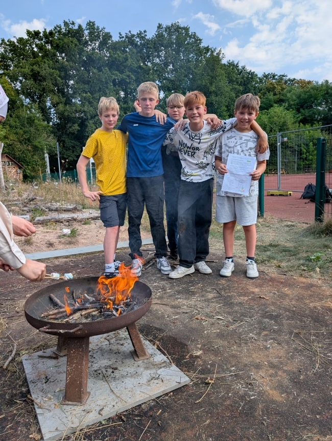 fünf Schüler stehen Arm in Arm zusammen vor einem Lagerfeuer