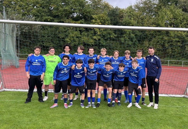 Gruppenbild mit Schulfussballern in blauen Trikots im Tor stehend mit Trainer