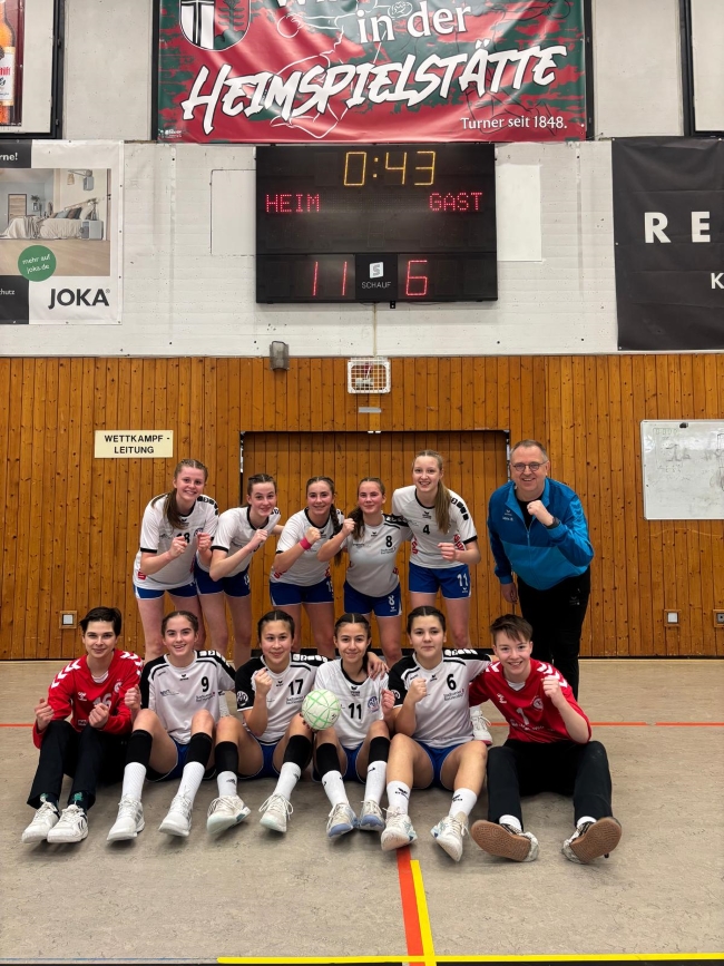 Gruppenfoto der Handballmädels mit Trainer jubelnd die Faust erhoben in einer Sporthalle