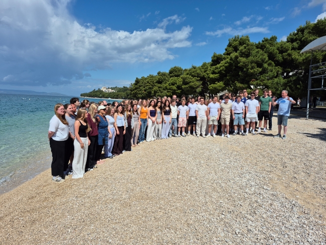 Chorschüler und Chorleiter am Strand bei blauem Himmel